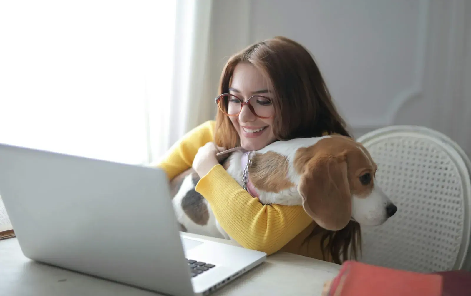 A woman in front of a computer, hugging a dog